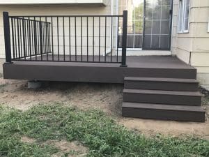 Small wooden deck off back slider door with a black railing